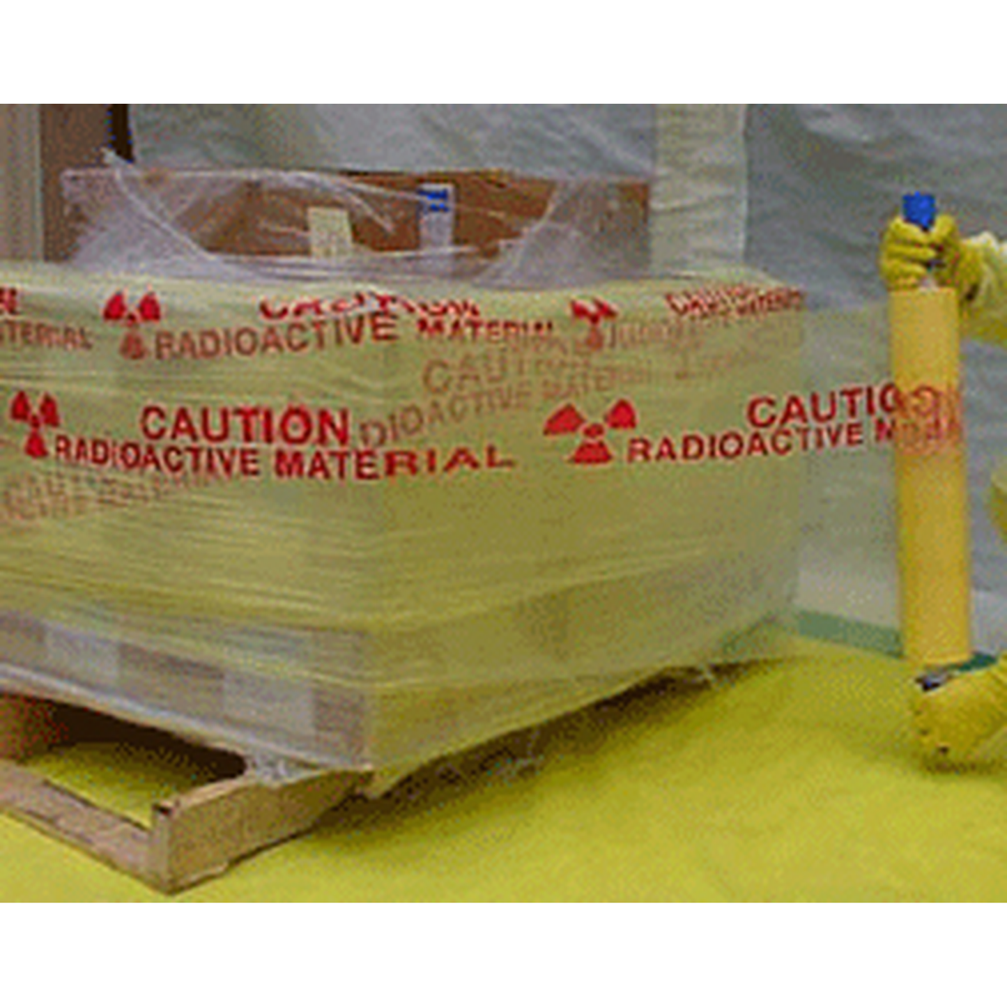 Stack of radioactive material containers with warning labels on a yellow surface.