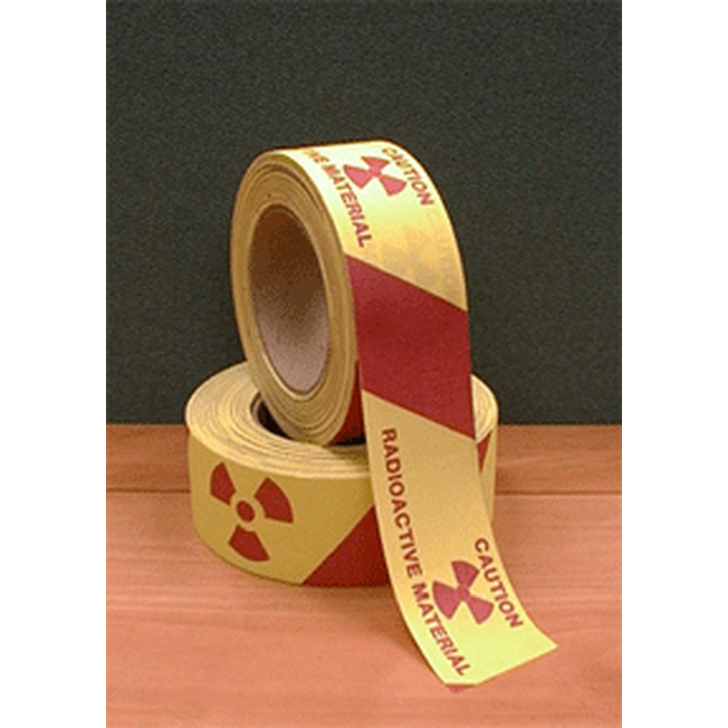 Two rolls of radioactive material warning tape on a wooden surface with a dark background.